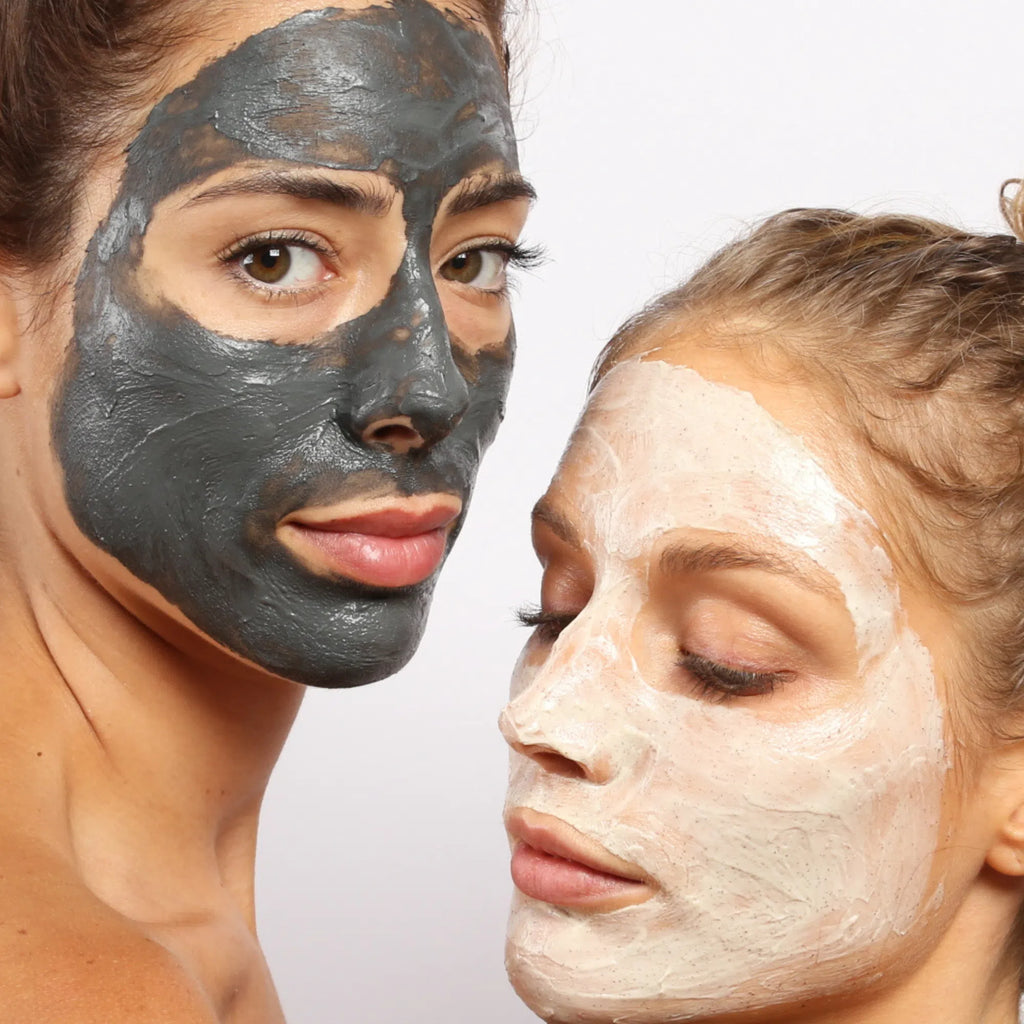 Zwei Frauen verwenden das DALUMA 2x MASK BUNDLE: eine trägt eine schwarze Kohlemaske und blickt in die Kamera, während die andere mit einer weißen Tonmaske nach unten blickt, beide vor einem hellen, schlichten Hintergrund.