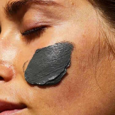 Eine Nahaufnahme des Gesichts einer Person mit geschlossenen Augen und einer dicken Schicht DALUMA CLEANSING AKTIVKOHLE FACE MASK auf der Wange - ideal für die natürliche Reinigung und Pflege.