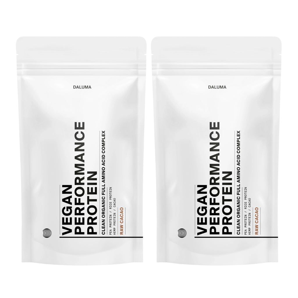 Zwei weiße, wiederverschließbare Beutel mit DALUMA VEGANES PERFORMANCE PROTEIN KAKAO DOUBLE stehen aufrecht und präsentieren diese vegane Bio-Proteinmischung mit minimalistischem schwarzem Text und dem Hinweis "Rohkakao" am Boden.