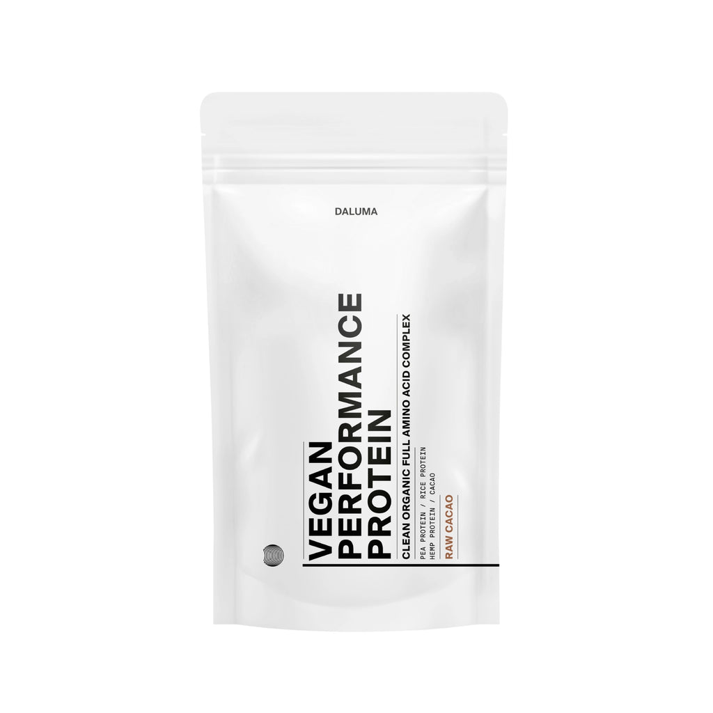 Ein weißer, wiederverschließbarer Beutel mit der Aufschrift VEGANES PERFORMANCE PROTEIN KAKAO" von DALUMA weist auf einer minimalistischen Verpackung mit schwarzem und orangefarbenem Text auf den vollen Aminosäurekomplex" und Rohkakao" hin, um dieses pflanzliche Protein hervorzuheben.