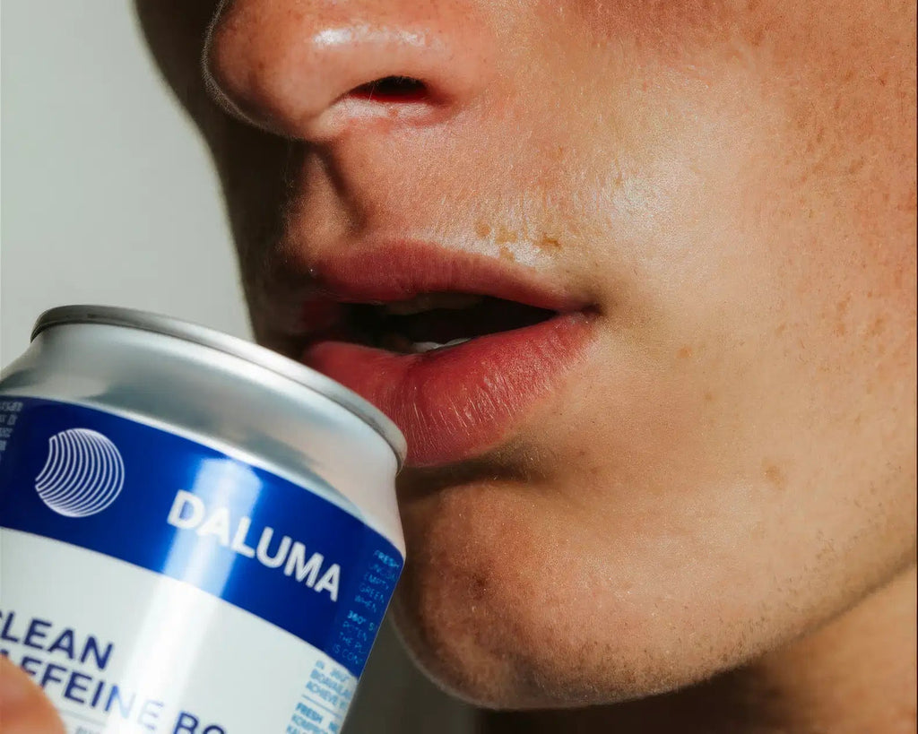 Eine Nahaufnahme einer Person mit geschürzten Lippen, die eine Dose mit der Aufschrift DALUMA an den Mund hält, deutet darauf hin, dass sie gleich ein CLEAN BCAA ENERGY DRINK aus dem 24 PACK genießen wird - ein Energy Drink mit veganen BCAAs.