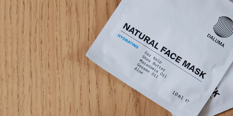 Ein weißes Säckchen mit der Aufschrift "Natural Face Mask" liegt auf einer Holzunterlage. Inhaltsstoffe wie Eichen-Seetang, Shea-Butter, Macadamia-Öl, Sesamöl und Aloe sind aufgeführt. Der Markenname "Daluma" und 18 ml Inhalt sind sichtbar.