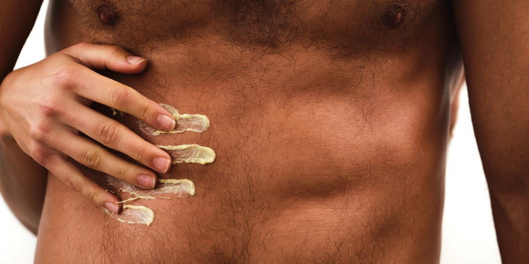 Nahaufnahme des nackten Oberkörpers eines Mannes mit einer Hand, die Creme oder Lotion in Streifen auf seinen Unterleib aufträgt.