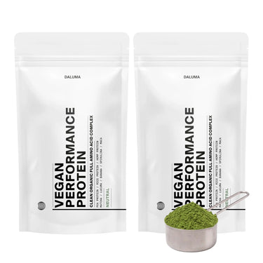 Zwei weiße DALUMA VEGANES PERFORMANCE PROTEIN NEUTRAL DOUBLE-Beutel stehen aufrecht nebeneinander, davor befindet sich eine Metallkugel mit neutralem pflanzlichem Proteinpulver.