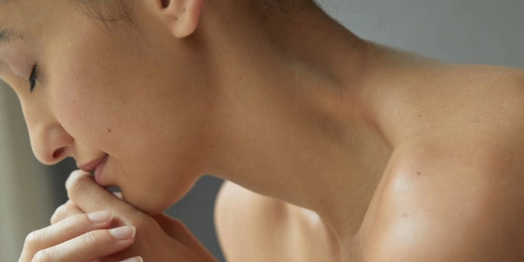 Nahaufnahme einer Frau mit nackten Schultern, die ihr Kinn auf die Hände stützt und ruhig und nachdenklich wirkt, wobei das weiche natürliche Licht ihren gelassenen Ausdruck hervorhebt.