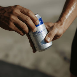 Zwei Hände sind zu sehen, die eine reicht eine kalte, blau-silberne CLEAN BCAA ENERGY DRINK 24 PACK von DALUMA an die andere. Das Kondenswasser auf der Dose unterstreicht die erfrischende Mischung aus natürlichem Koffein und veganen BCAAs.