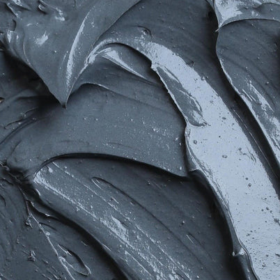 Nahaufnahme der CLEANSING AKTIVKOHLE FACE MASK von DALUMA: eine glatte, dicke, dunkelgraue Substanz mit cremiger Textur und sichtbaren Schlieren.