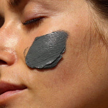 Nahaufnahme des Gesichts einer Person mit geschlossenen Augen, auf deren Wange eine glatte Schicht der DALUMA CLEANSING AKTIVKOHLE FACE MASK aufgetragen ist. Die Haut sieht sauber und gesund aus.