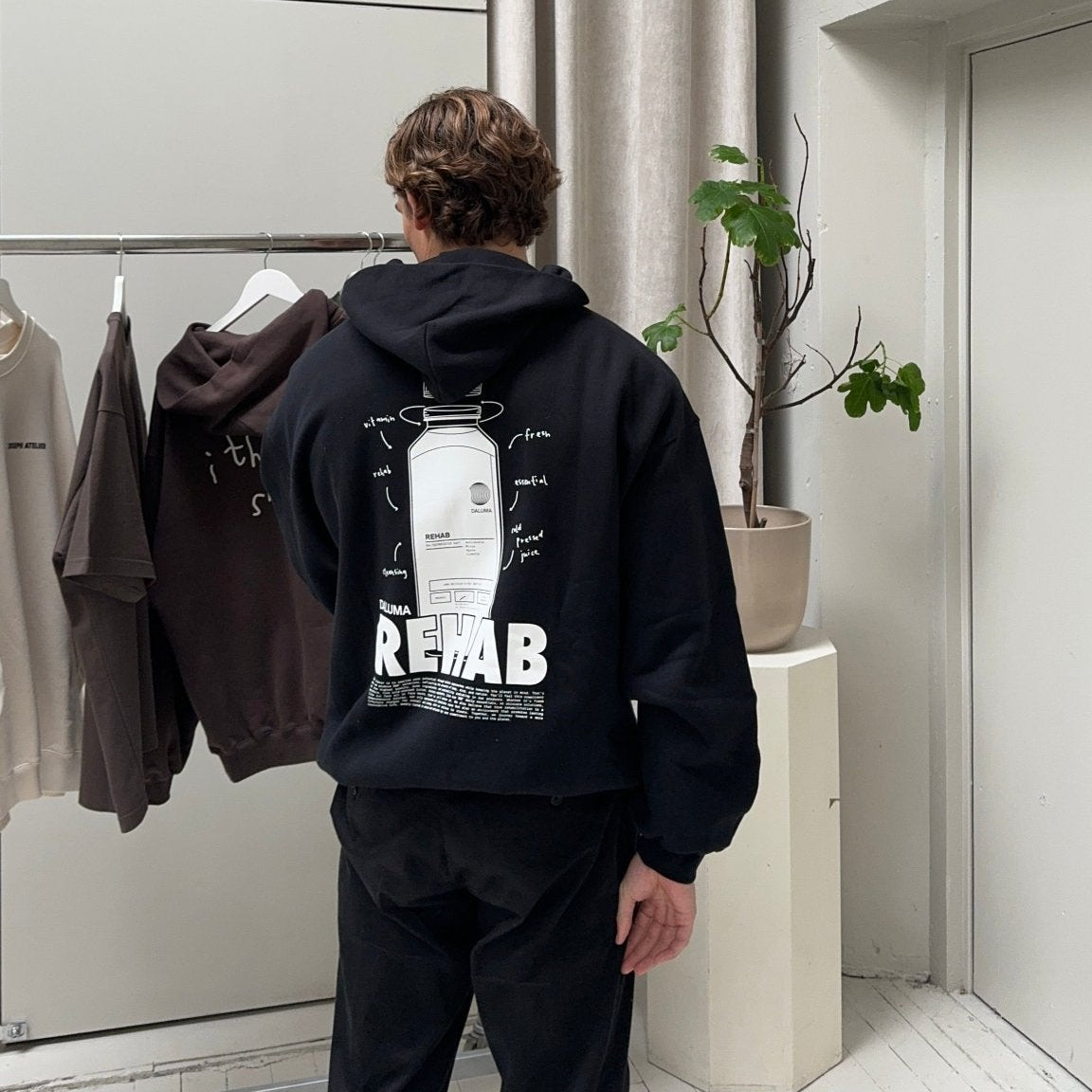 Eine Person mit kurzen braunen Haaren trägt den DALUMA JOSEPH ATELIER X DALUMA REHAB HOODIE mit einer Grafik und dem Text 