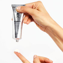Eine Hand hält eine silberne Tube DALUMA FACIAL MOISTURIZER GESICHTSPFLEGE, während eine andere eine kleine Menge auf einem Zeigefinger sammelt, geeignet für alle Hauttypen, vor einem weißen Hintergrund.