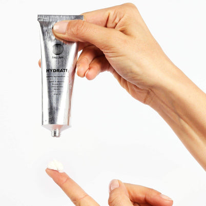 Eine Hand drückt eine kleine Menge DALUMA FACIAL MOISTURIZER GESICHTSPFLEGE aus einer silbernen Tube auf einen Zeigefinger und gibt natürliche Feuchtigkeit vor weißem Hintergrund ab.