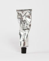 Eine zerknitterte silberne Tube mit schwarzer Kappe, auf der FACIAL MOISTURIZER GESICHTSPFLEGE und DALUMA steht, ruht auf einem schlichten weißen Hintergrund - eine elegante Feuchtigkeitscreme für das Gesicht und natürliche Feuchtigkeitscreme für jeden Hauttyp.