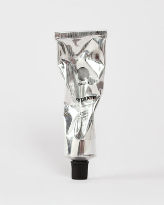 Eine zerknitterte silberne Tube mit schwarzer Kappe und der Aufschrift DALUMA FACIAL MOISTURIZER GESICHTSPFLEGE ruht auf einem schlichten weißen Hintergrund - eine elegante Feuchtigkeitscreme für das Gesicht, die für höchste Qualität und natürliche Feuchtigkeitszufuhr entwickelt wurde.
