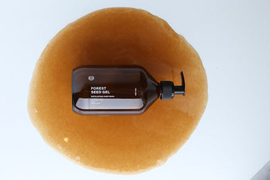 Eine braune Pumpflasche mit DALUMA FOREST SEED GEL HAND WASH steht auf einer Lache aus karamellfarbenem Gel und hebt dieses Handwaschmittel mit natürlichen Inhaltsstoffen für sanfte Hautpflege hervor.