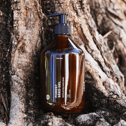 Eine Pumpflasche aus braunem Glas mit der Aufschrift DALUMA FOREST SEED GEL HAND WASH lehnt sich an die Wurzeln eines Baumes und hebt die natürlichen Inhaltsstoffe hervor, die umweltfreundliche und von der Natur inspirierte Themen miteinander verbinden.
