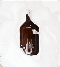 Eine braune Flasche mit der Aufschrift DALUMA FOREST SEED GEL HAND WASH mit weißer Schrift ruht auf einer weißen, mit Seifenlauge gefüllten Fläche und hebt Handseife mit natürlichen Inhaltsstoffen für sanfte Hautpflege hervor.