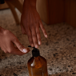 Die Hände drücken auf die Pumpe eines DALUMA FOREST SEED GEL HAND WASH-Spenders, der aus natürlichen Inhaltsstoffen hergestellt wird, und die Flasche steht auf einer gesprenkelten Arbeitsplatte.