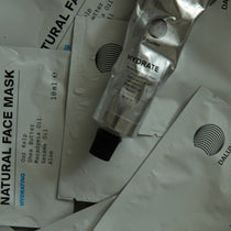 Eine Tube mit der Aufschrift HYDRATING ESSENTIALS ruht auf einer weißen Verpackung mit der Aufschrift DALUMA, auf der Wassertropfen sichtbar sind.