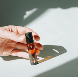 Eine Hand hält ein kleines Braunglas-Tropffläschchen mit der Aufschrift NULLPUNKT GRADE 0.3 REFOCUS von Nullpunkt und einer schwarzen Kappe, die einen weichen Schatten auf eine weiße Fläche in hellem Tageslicht wirft.