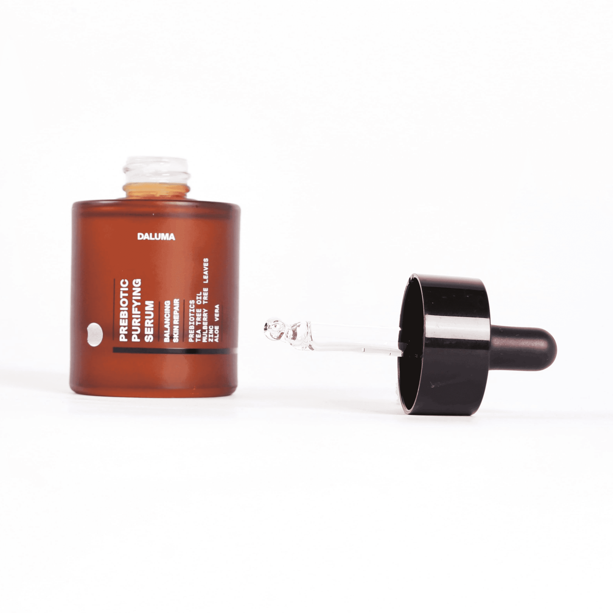 Eine geöffnete bernsteinfarbene Flasche DALUMA PREBIOTIC PURIFYING GESICHTSSERUM mit schwarzem Tropfverschluss ist auf weißem Hintergrund abgebildet und hebt Unreinheiten Reduktion und probiotische Bakterienkulturen zur Unterstützung der Hautbarriere hervor.