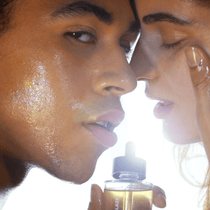 Zwei Menschen mit strahlender, taufrischer Haut stehen sich direkt gegenüber. Die eine hält ein Fläschchen FACE GLOW DUO von DALUMA an die Lippen, die andere berührt sanft ihr Gesicht, die Augen geschlossen, bei sanfter Beleuchtung.