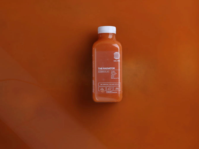 Eine mit orangefarbener Flüssigkeit gefüllte Plastikflasche mit der Aufschrift The Radiator steht mittig auf einem orangefarbenen Hintergrund, der sich in die Umgebung einfügt. Das Etikett enthält kleinen weißen Text und Grafiken.