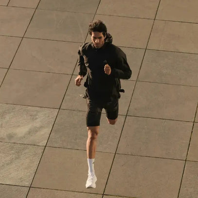 Ein Mann in schwarzer Sportkleidung und weißen Turnschuhen läuft auf einem großen gefliesten Pflaster, von oben gesehen.